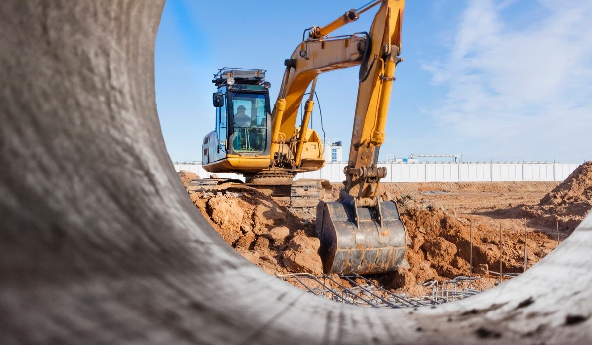 Excavator on a dig site seen through a large concrete culvert pipe