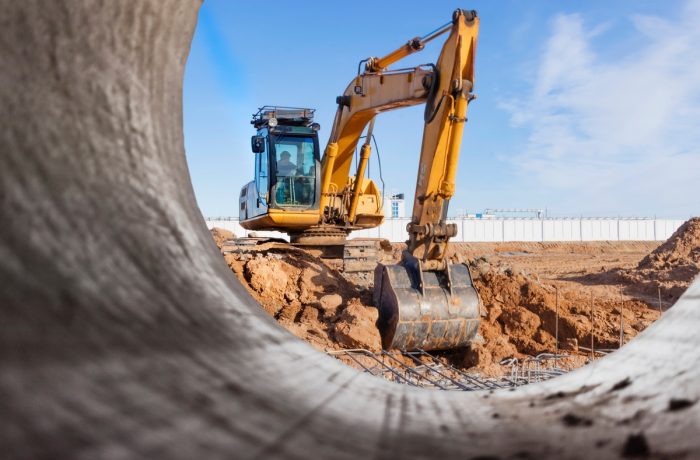 Excavator on a dig site seen through a large concrete culvert pipe