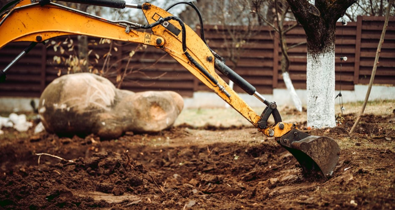 Excavator moving a large boulder in a backyard