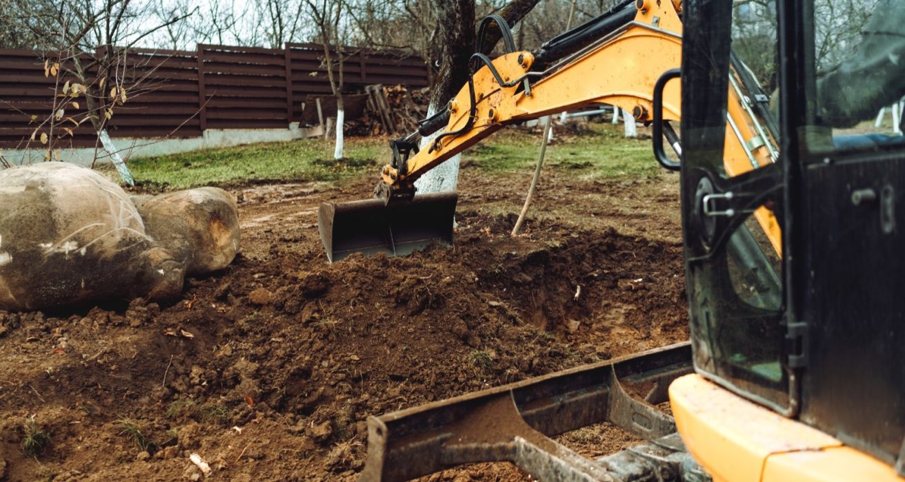 Mini excavator grading soil beside a large boulder