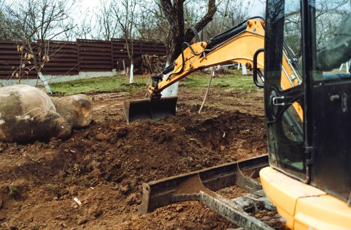 Mini excavator grading soil beside a large boulder