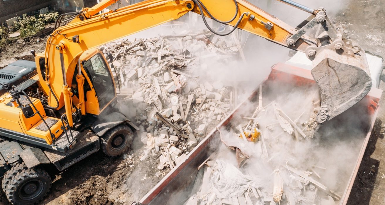 Excavator loading demolition rubble into a disposal bin