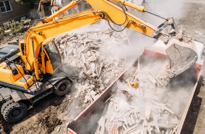 Excavator loading demolition rubble into a disposal bin